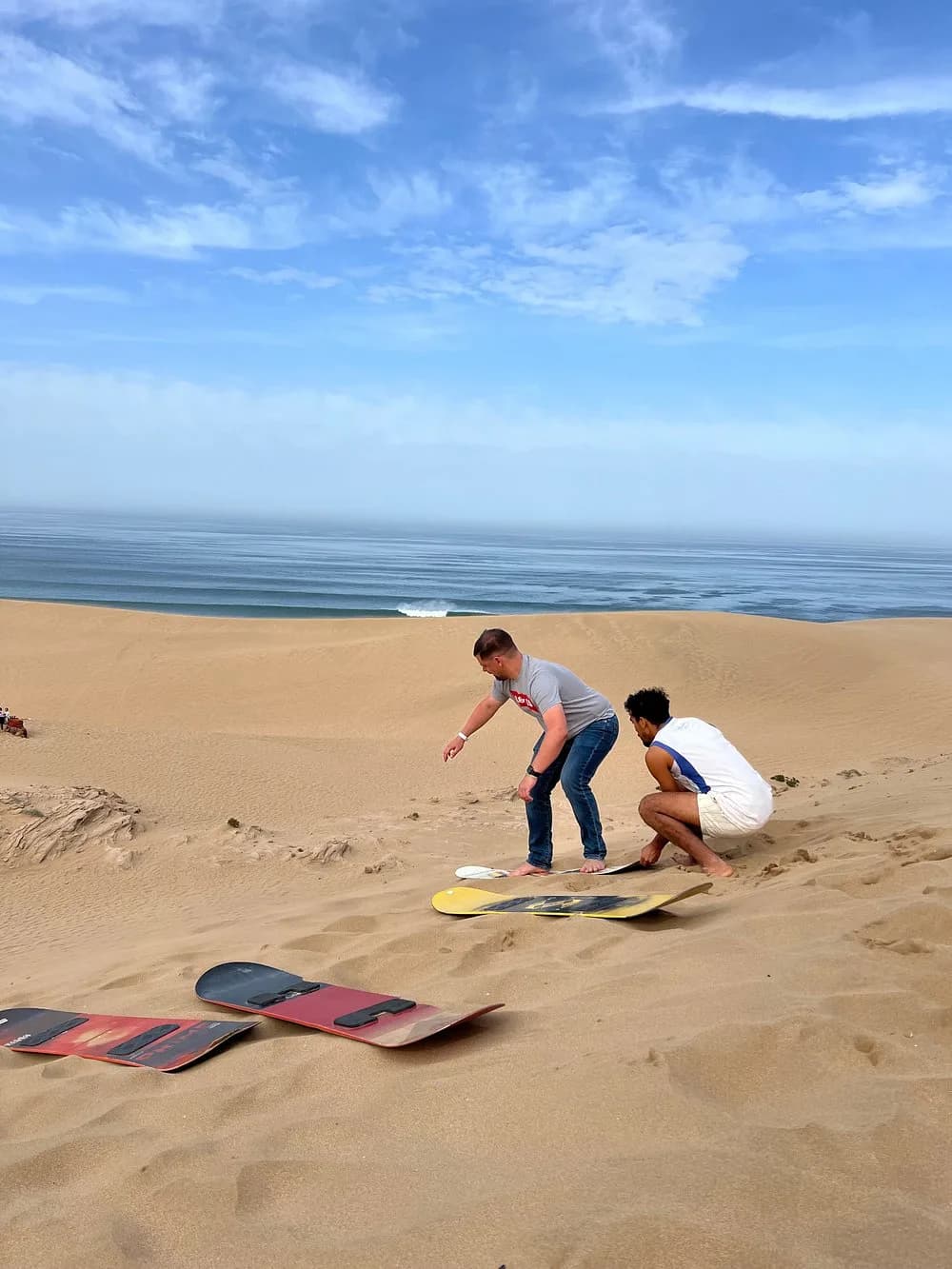 A local guide teaching a traveller to sandboard on the dunes above the Atlantic